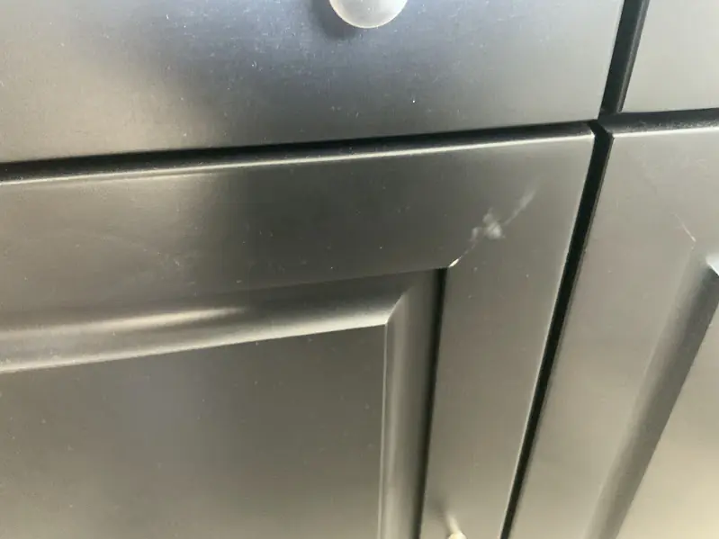 Before photo of a cabinet door with a scratch and scuff, prior to repair.