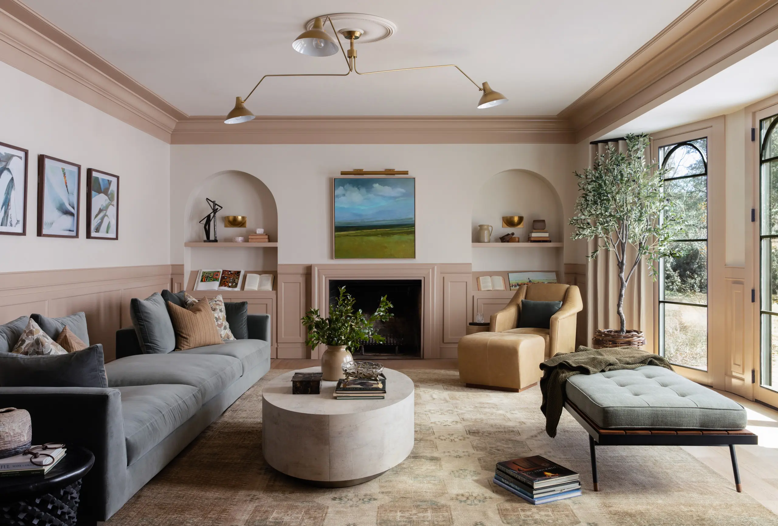Warm high-end living room with gray velvet sectional, tan leather armchair and ottoman, round stone coffee table, and fireplace