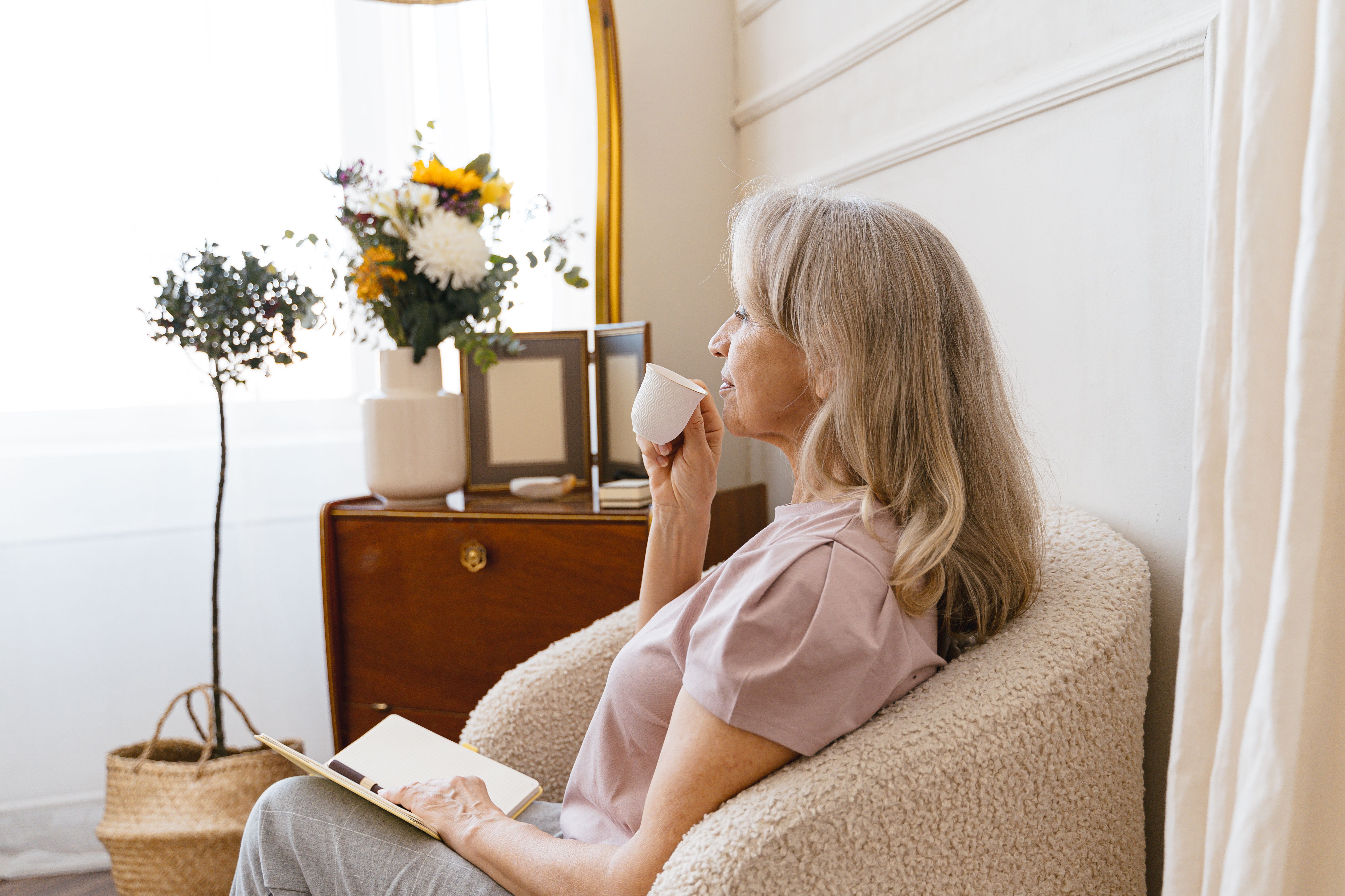 Midlife woman with morning coffee by a window representing the quiet intentional start to a day that belongs to her. Midlife woman with morning coffee by a window representing the quiet intentional start to a day that belongs to her.
