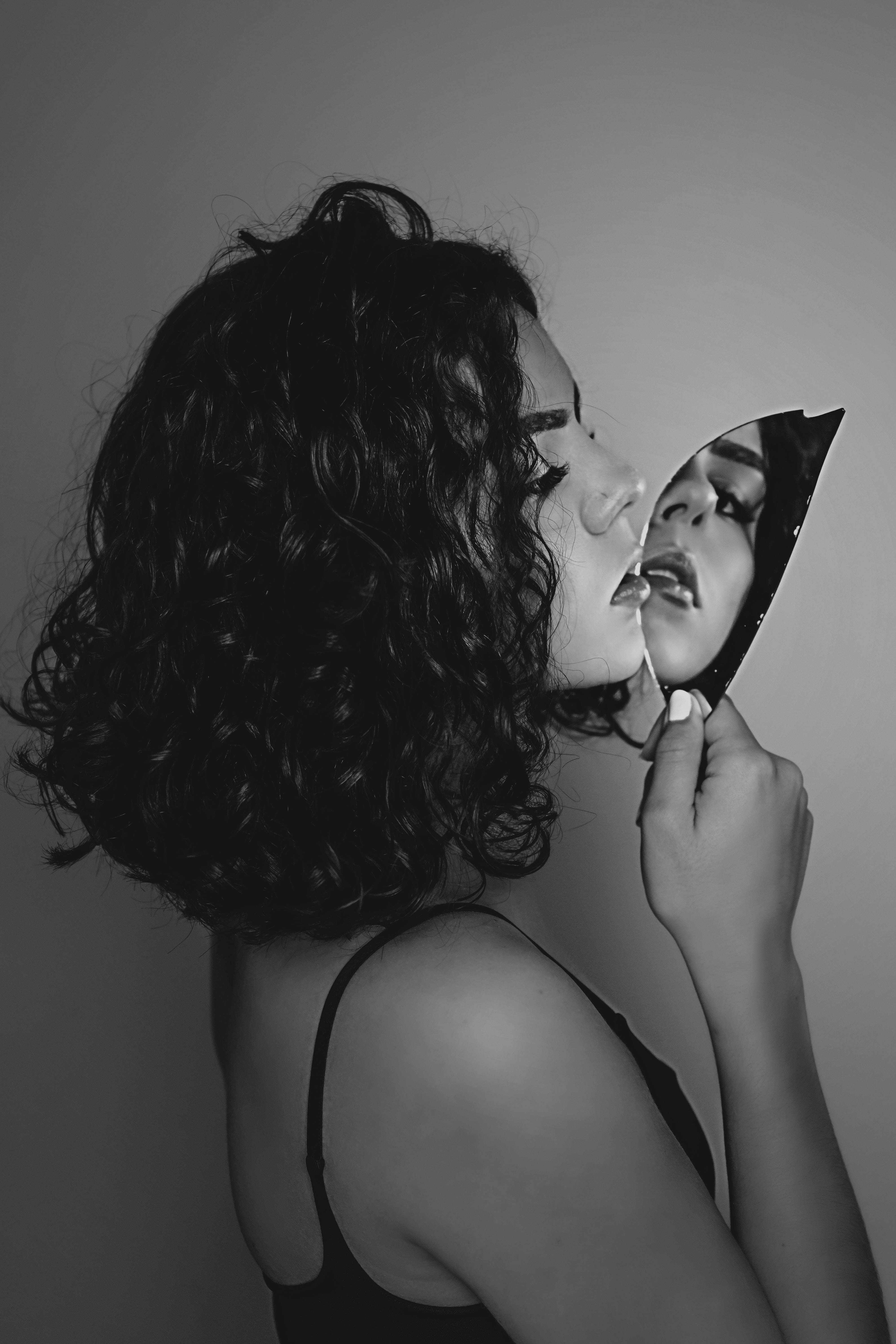 Black and white photo of woman looking into a broken shard of mirror and making contact with camera lens through mirror