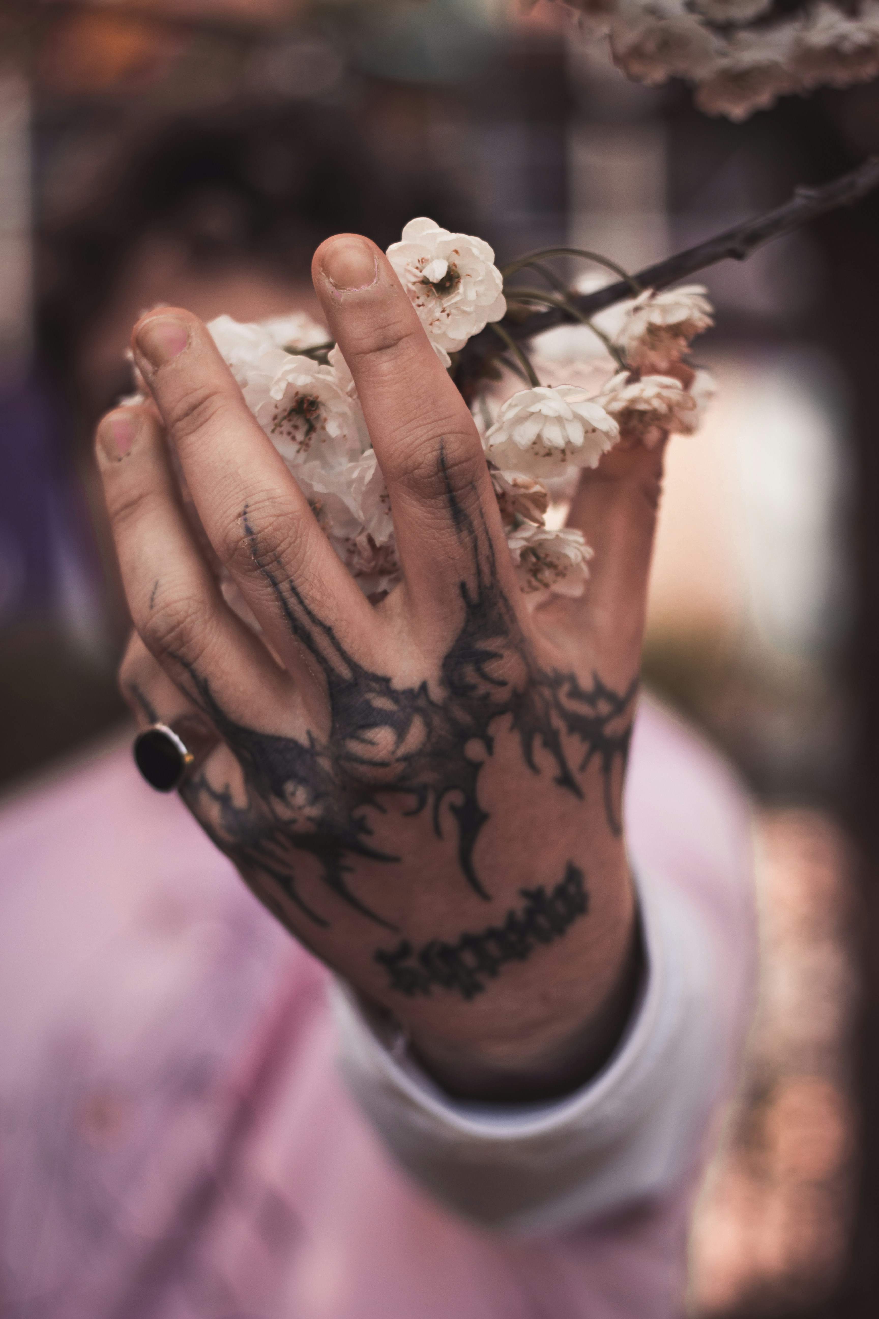 Tattoed hand gently holding white bloosom flowers close to camera and background blurry