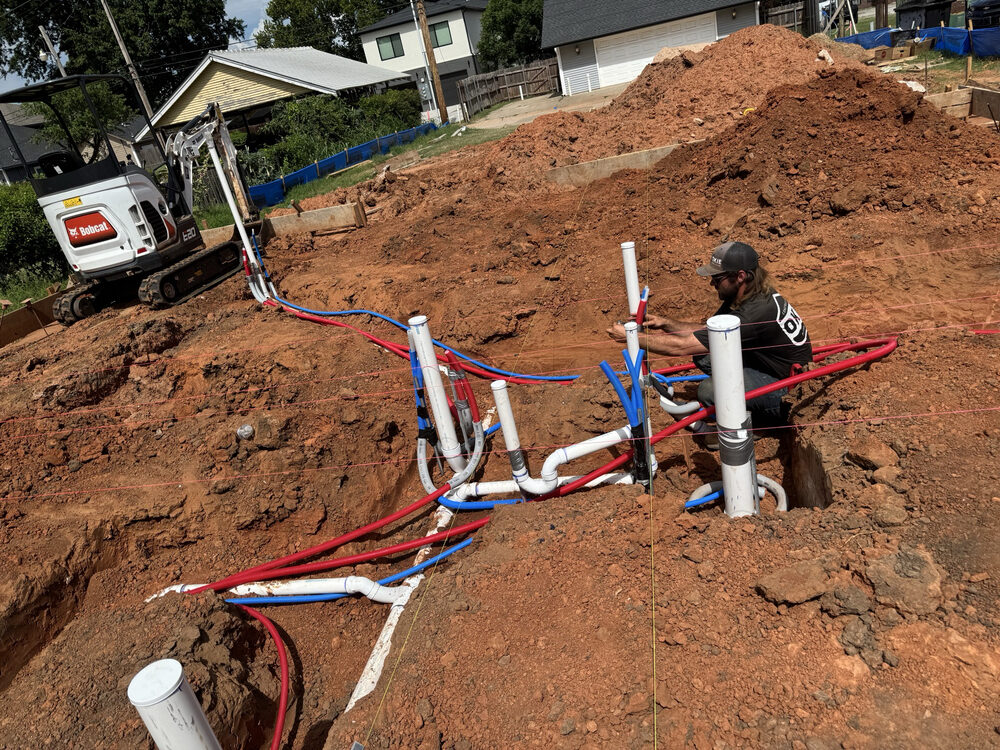 Plumber setting PEX and PVC rough-in on red dirt at a new home site