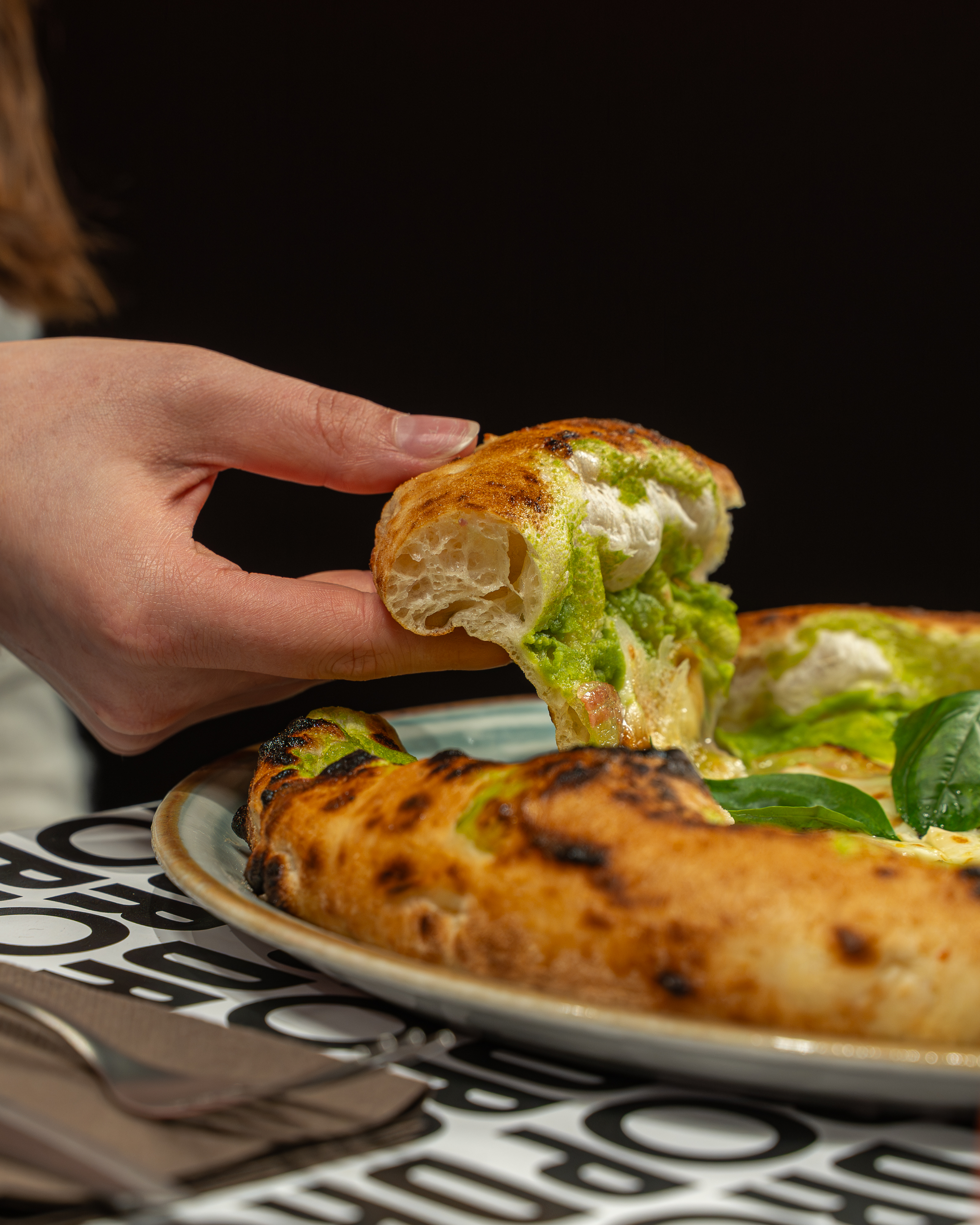 Una fetta di pizza DROP sollevata dal piatto, con il cornicione alveolato in primo piano