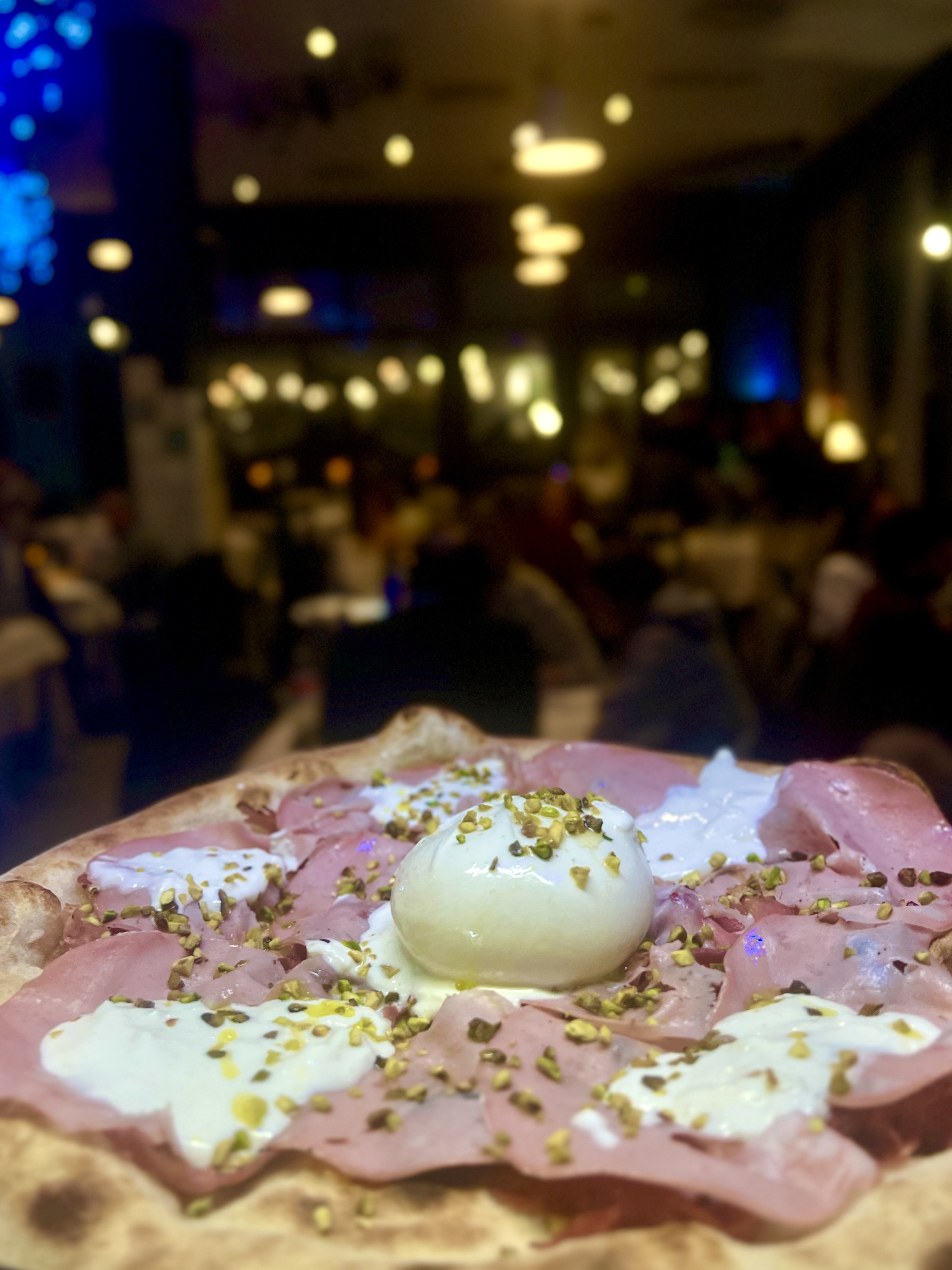Pizza Sanfy con mortadella, burrata e granella di pistacchio nella sala illuminata