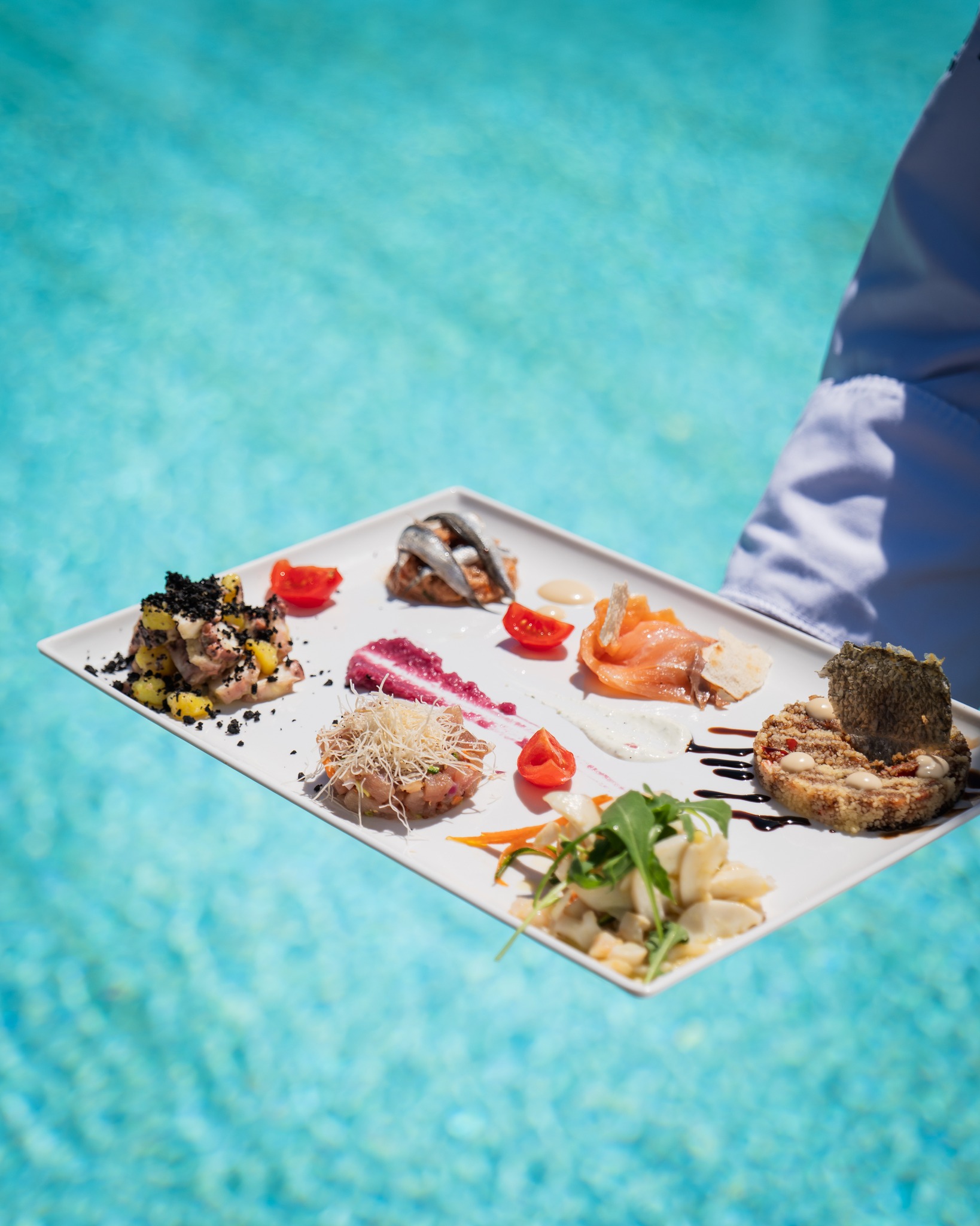 Una selezione di antipasti di pesce servita accanto all’acqua turchese della piscina di Acquapazza