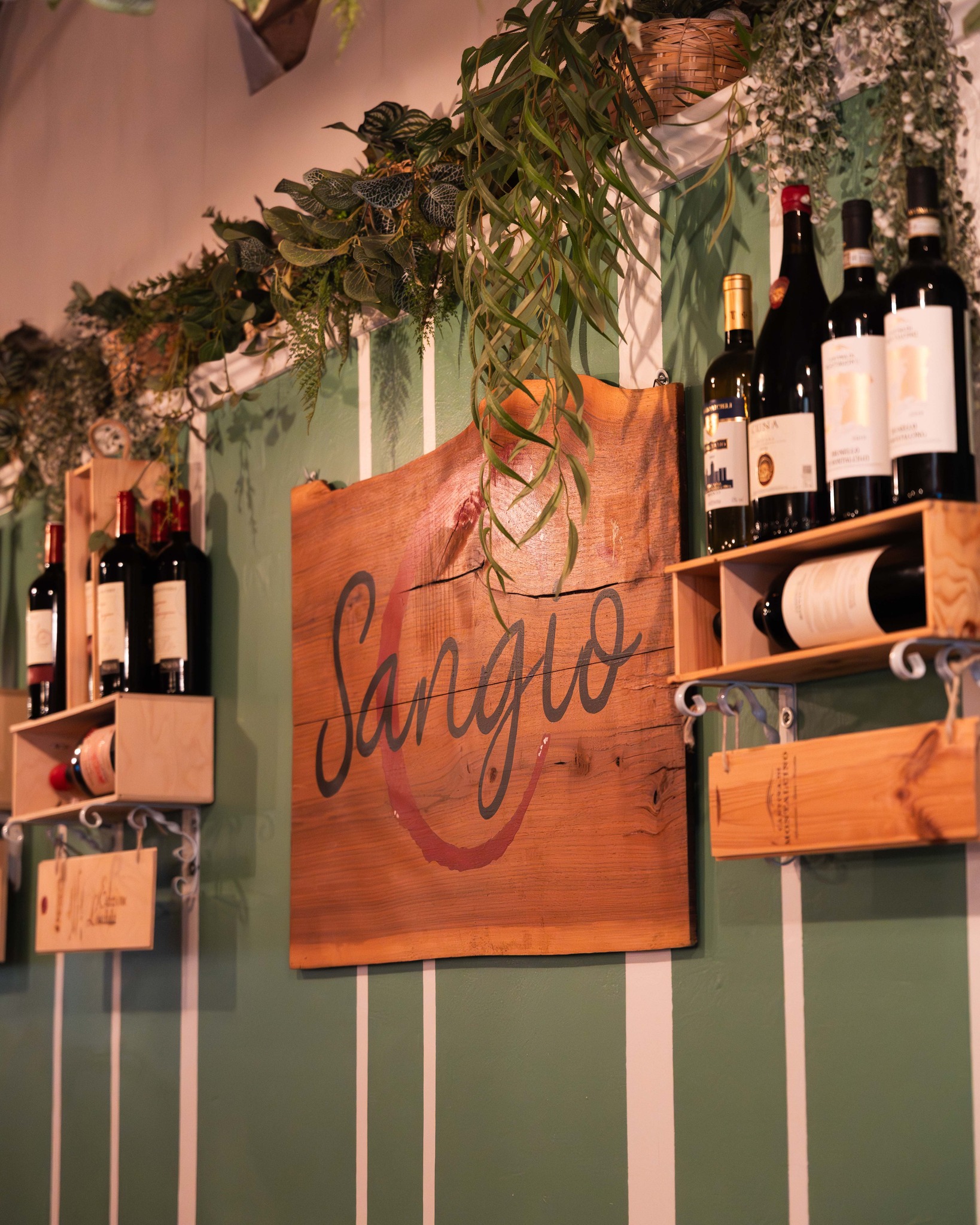 Insegna in legno Sangiò tra piante e bottiglie di vino