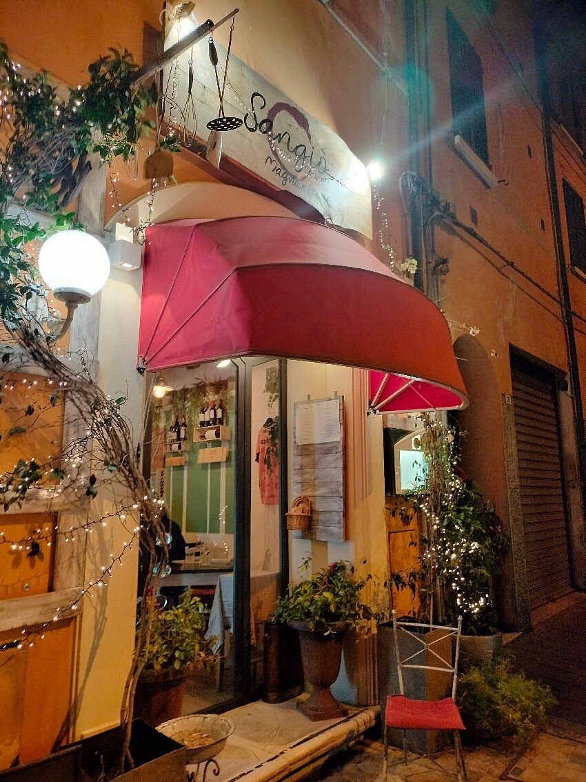 Ingresso di Al Sangiò illuminato la sera, con tenda rossa e piante