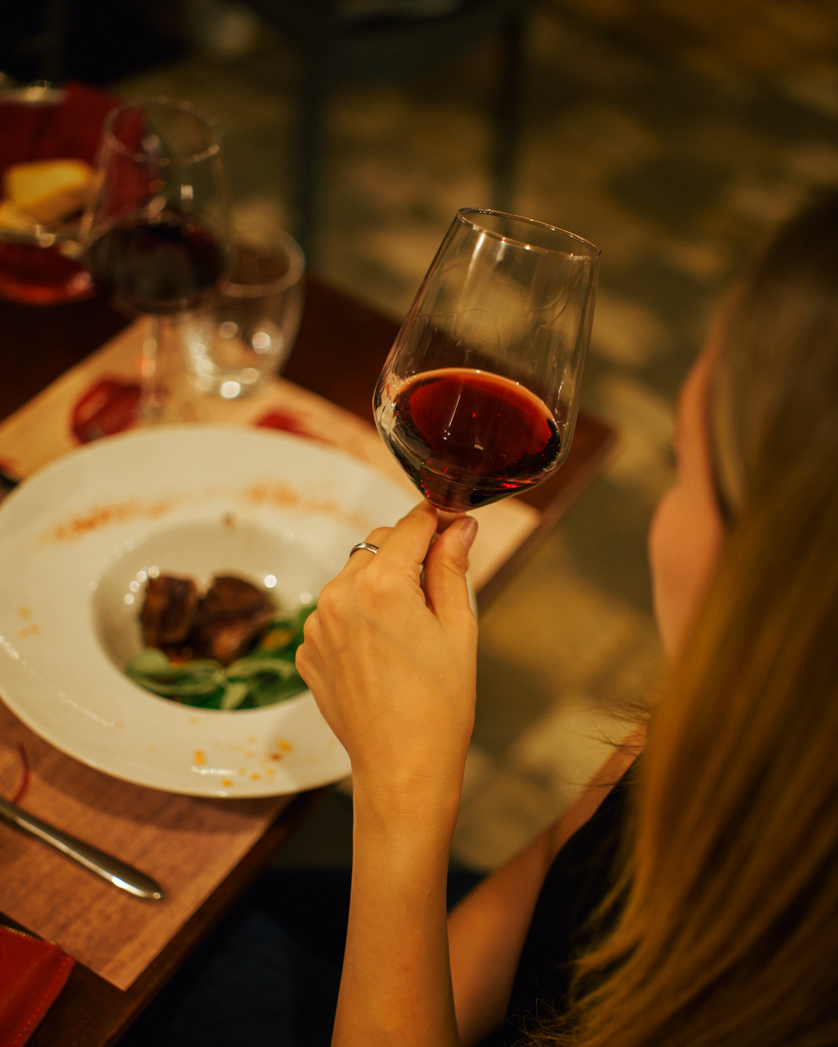 Una donna con un calice di vino rosso davanti a un piatto