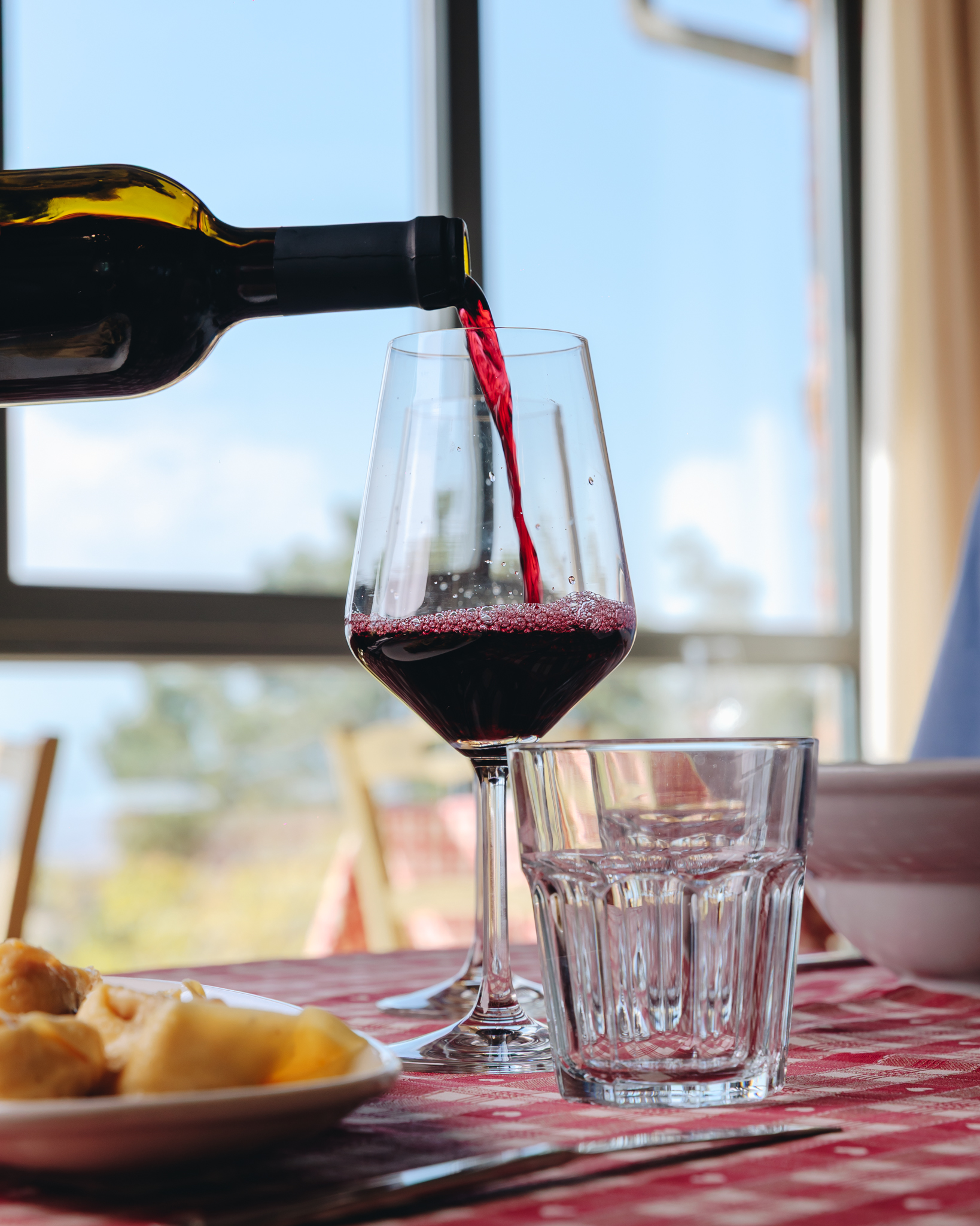 Un calice di vino rosso servito a tavola davanti al panorama delle colline