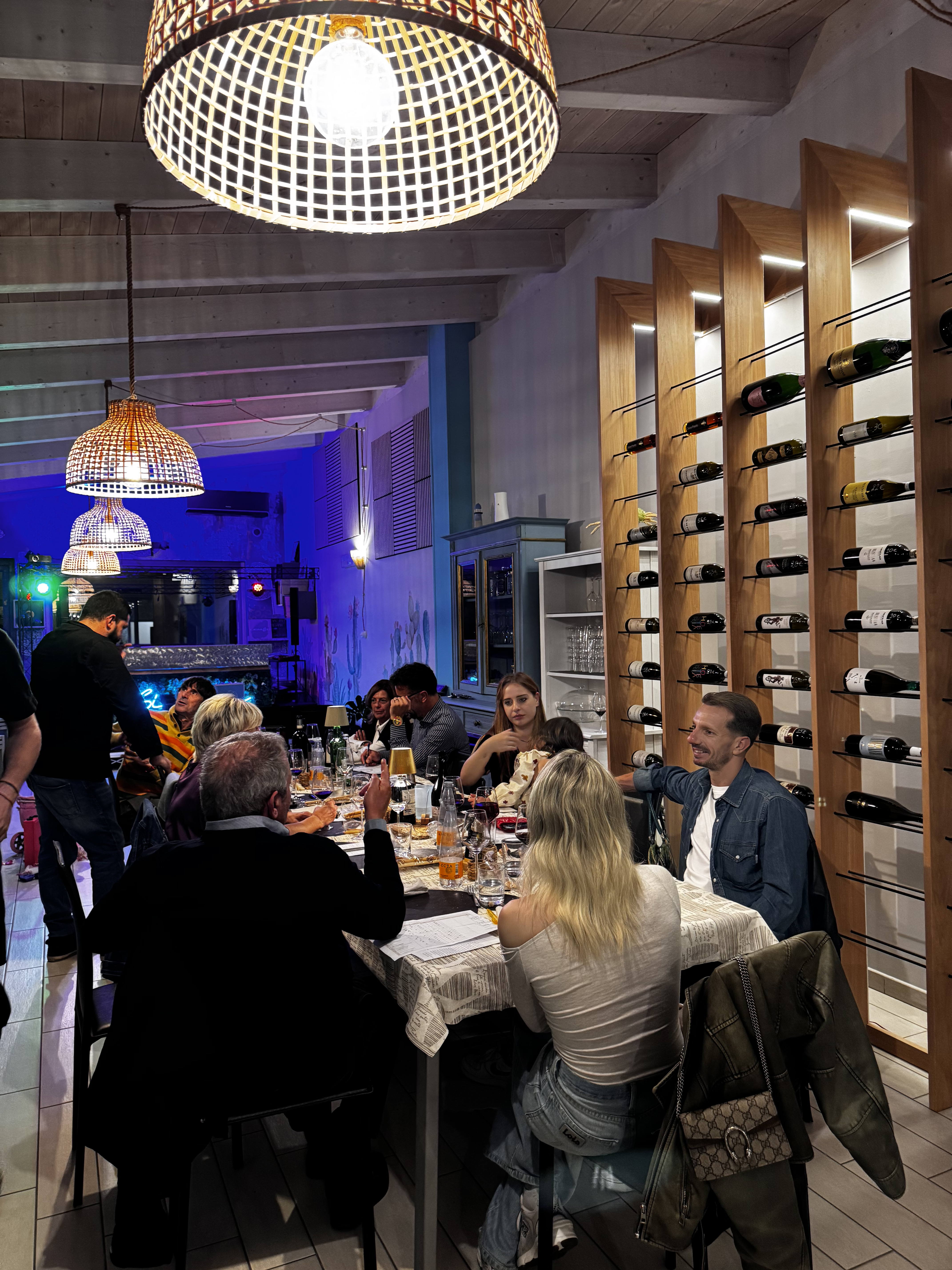 Una cena in compagnia nella sala di Sibilla, tra lampade intrecciate e la parete dei vini