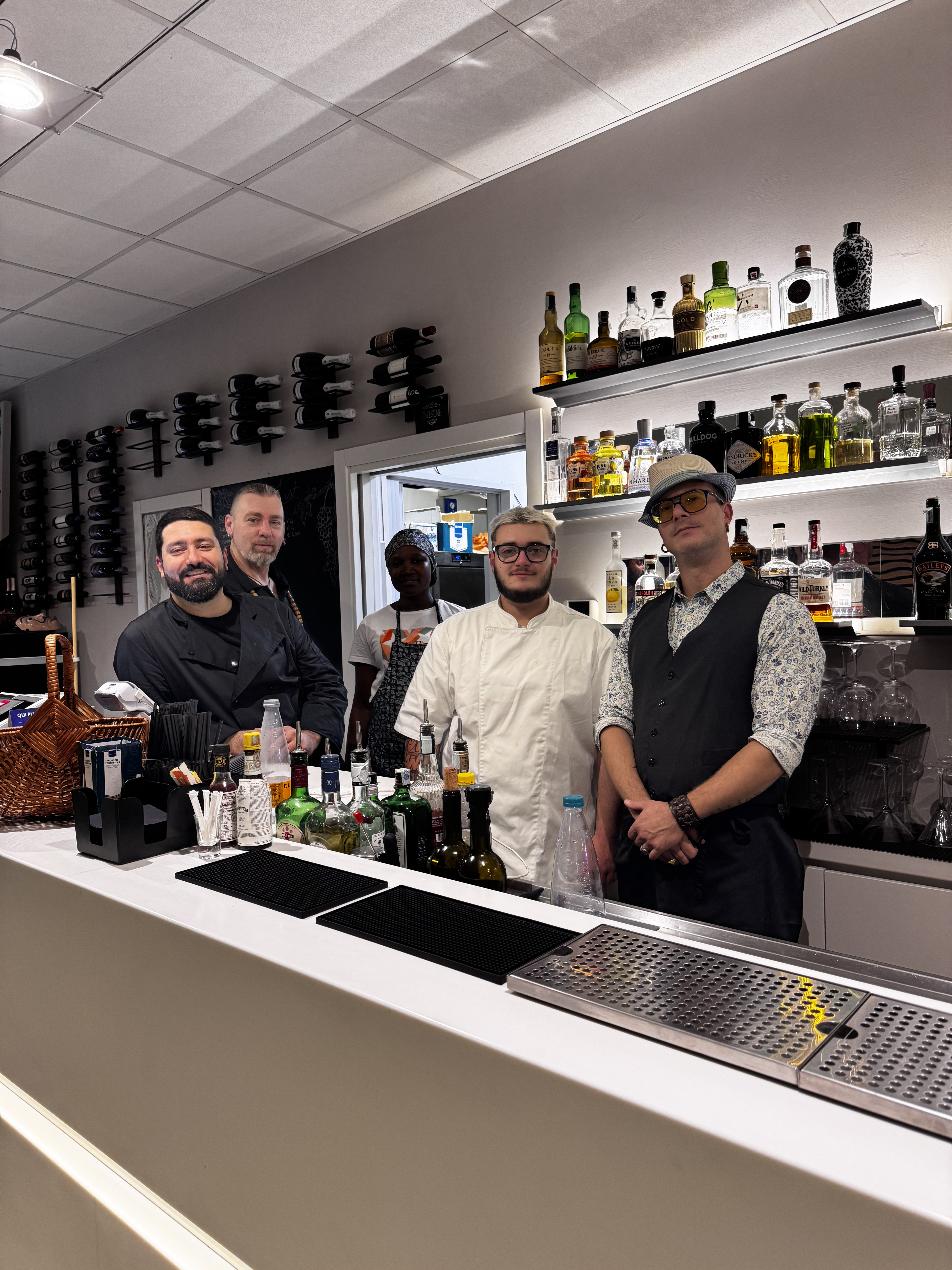 Il team di Sibilla dietro il bancone del bar, con la bottigliera illuminata alle spalle