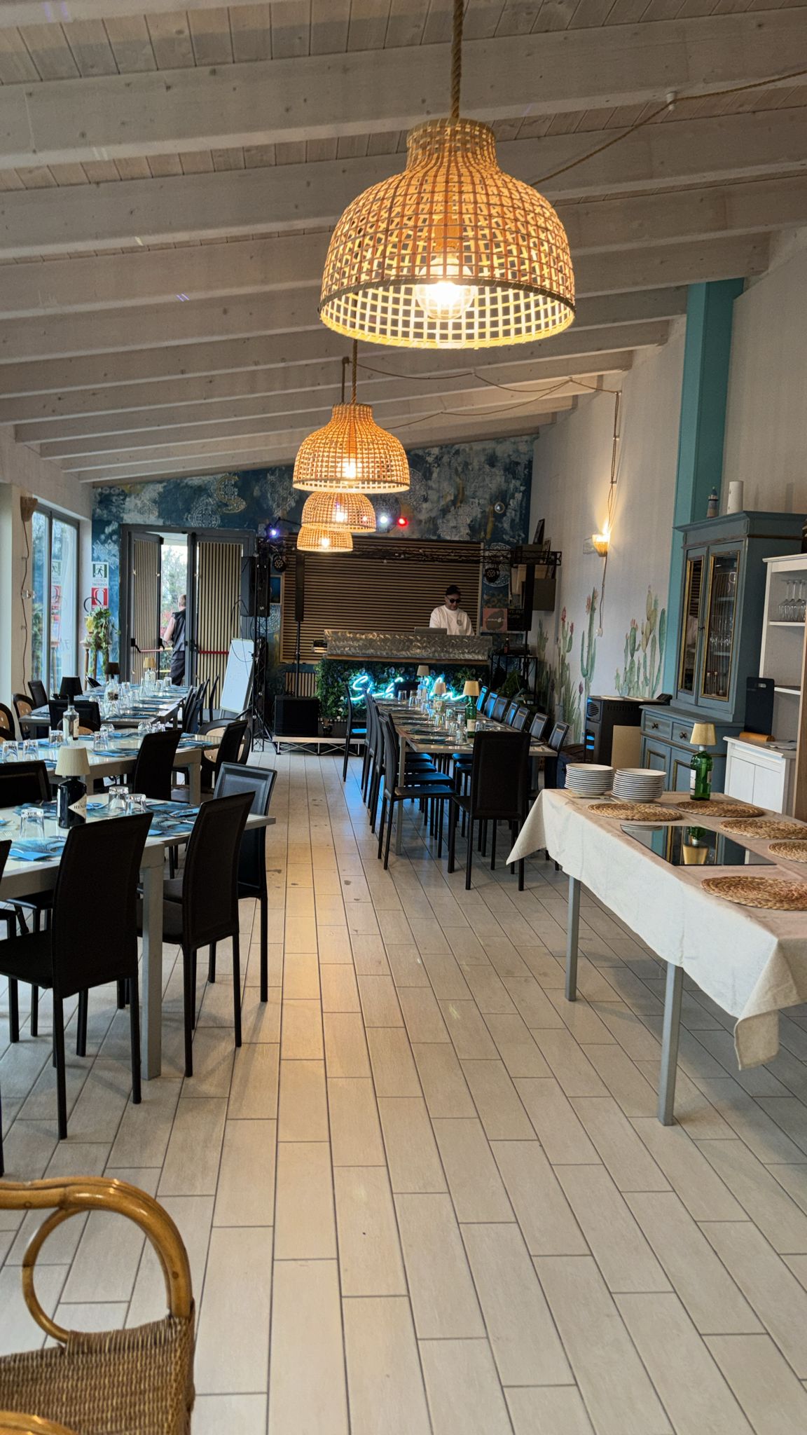 La sala di Sibilla vista dall'ingresso, con tavoli apparecchiati, lampade intrecciate e il bar sul fondo