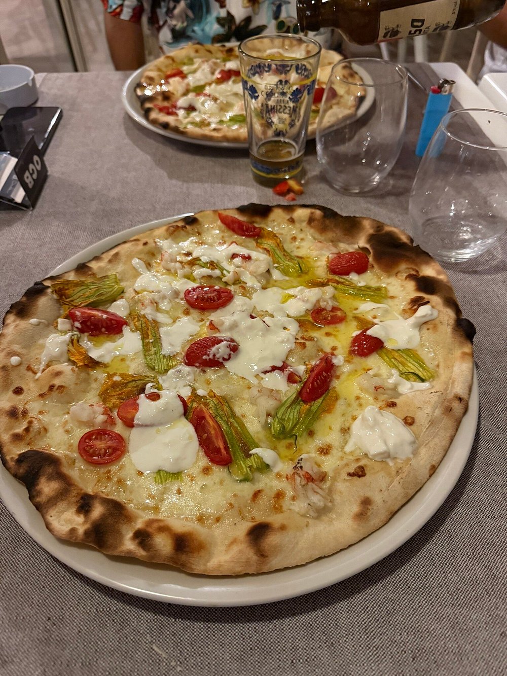 Pizza con fiori di zucca, pomodorini e stracciatella servita al tavolo