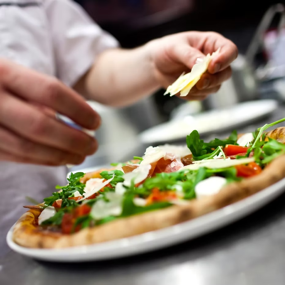 La preparazione di una pizza con rucola, pomodorini e scaglie di formaggio nella cucina de La Dolce Vita