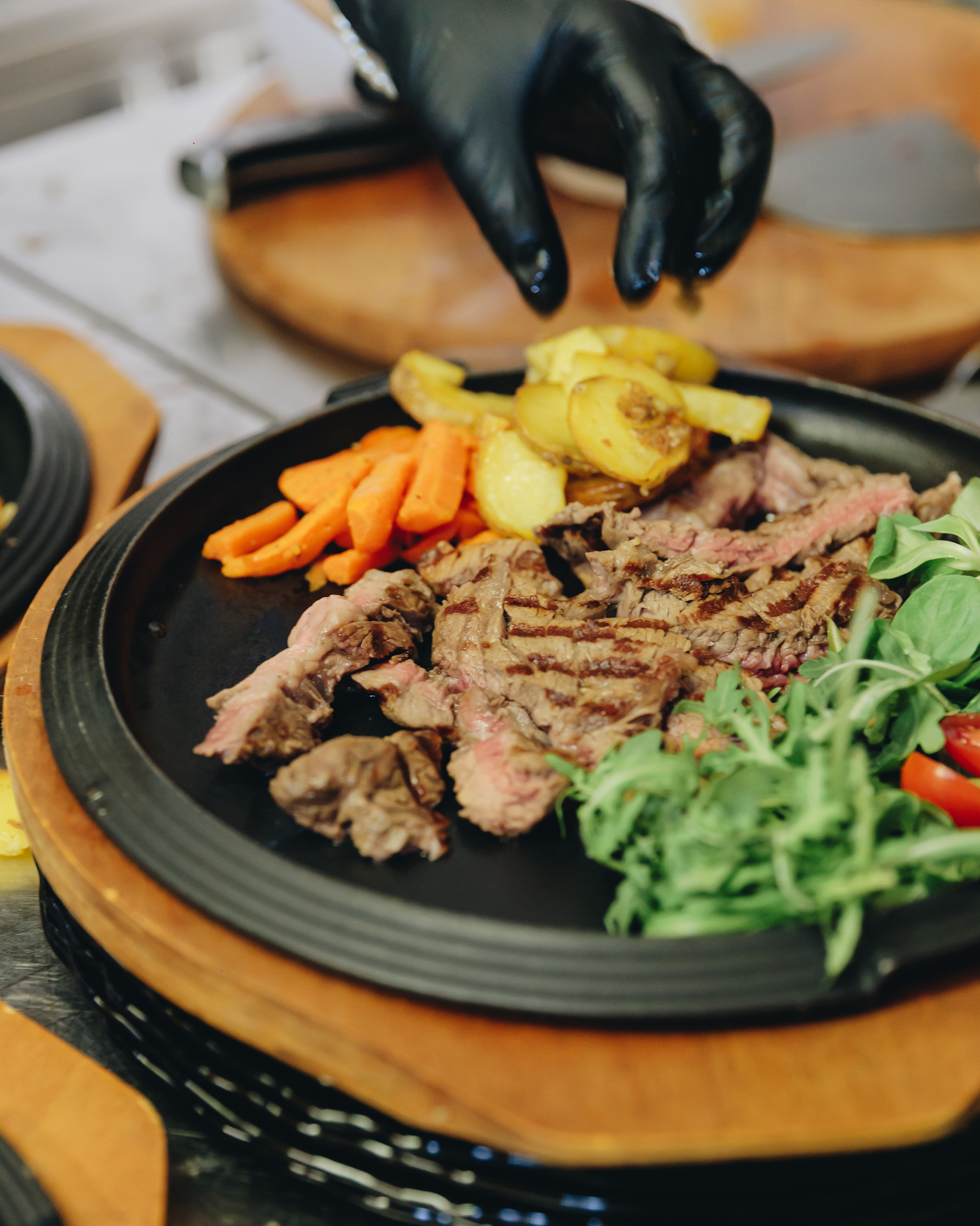 Tagliata servita su piastra con patate, carote e rucola