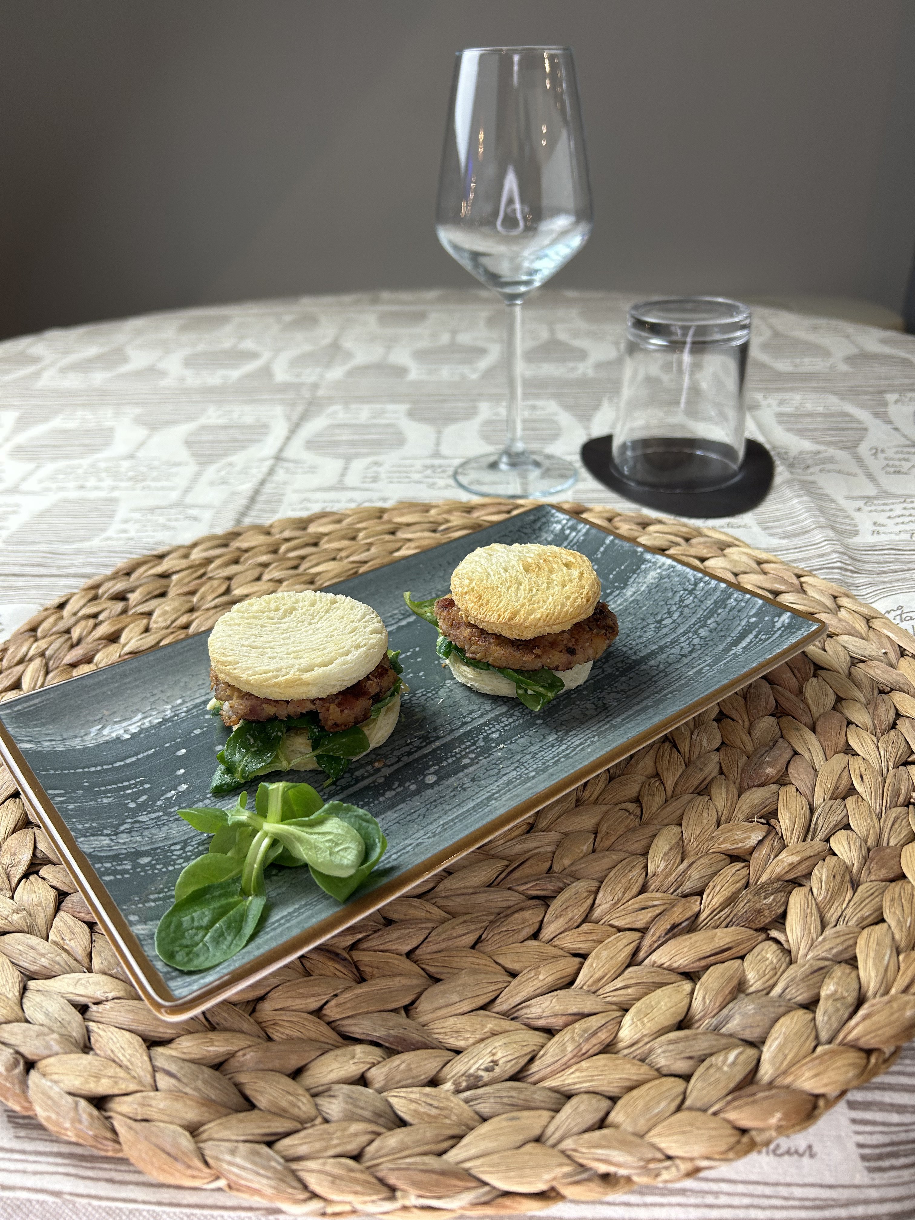 Mini rösti farciti serviti su un piatto in ceramica, con un calice di vino sullo sfondo