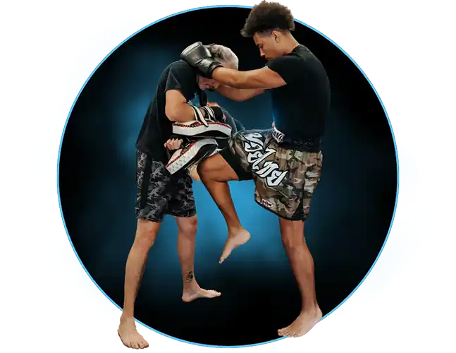 Two men training Muay Thai in a Port Orange, Florida gym; the younger fighter is clinching his opponent and delivering a knee strike