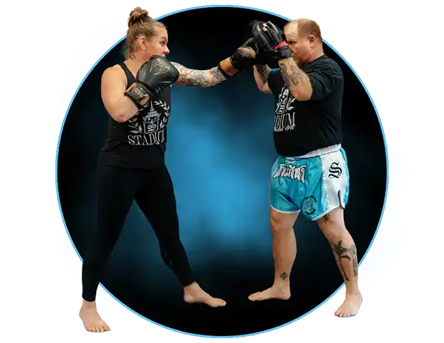 A man and woman practice kickboxing at Stadium MMA in Port Orange, Florida, with the man holding pads while the woman throws punches, honing both fitness and technique