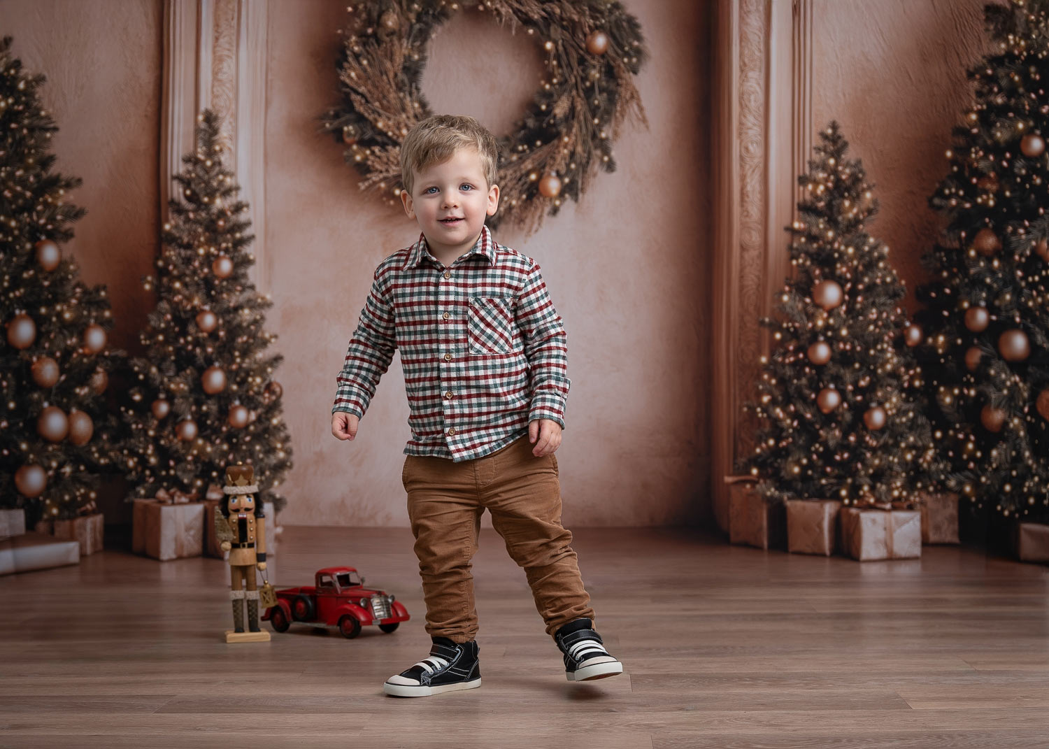 Young boy holiday portrait with Christmas trees and wreath