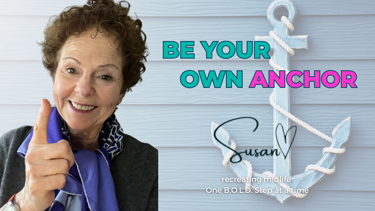 A woman with short, curly brown hair smiles and points her finger upward in this horizontal digital graphic. She wears a dark grey top and a blue patterned silk scarf.  To the right, a large, light blue wooden anchor wrapped in white rope is set against a light blue wood-paneled background. The text "BE YOUR OWN ANCHOR" is displayed in bold teal and pink capital letters. Below it, a black script signature reads "Susan" with a small heart, followed by the tagline: "recreating midlife One B.O.L.D. Step at a time."
