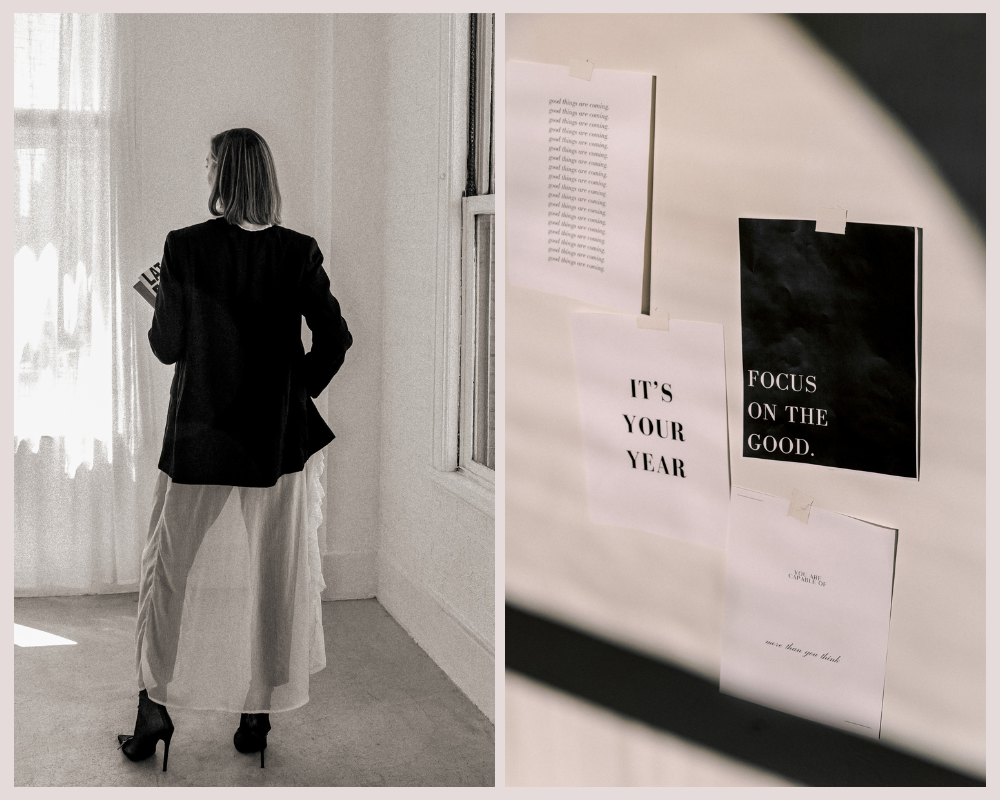 Woman standing in a bright studio holding a notebook, with inspirational affirmations on the wall.