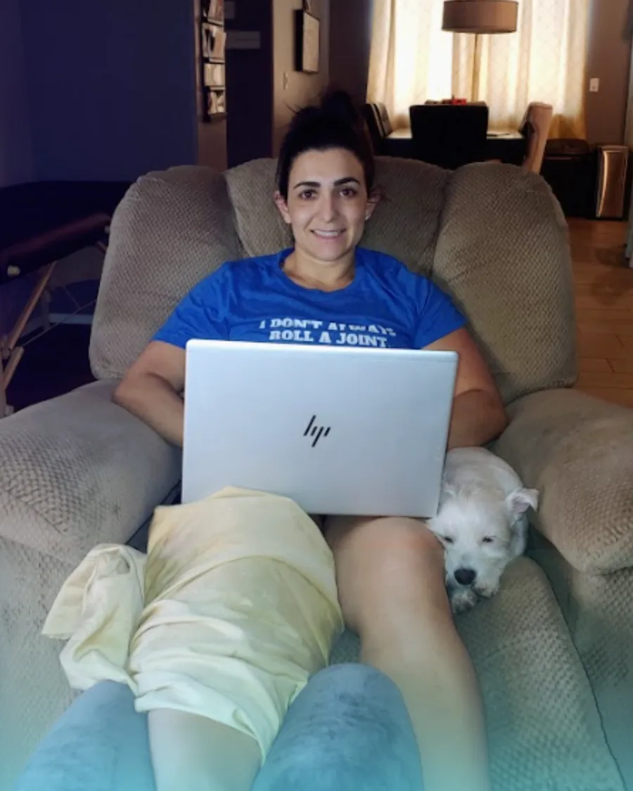 Dr. Christina recovering at home in a recliner after knee surgery, laptop on her lap and her dog beside her