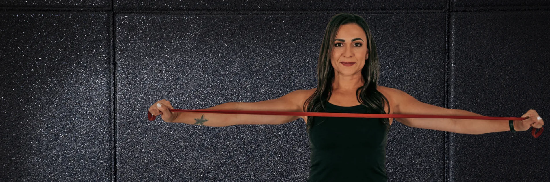 Dr. Christina stretching a red resistance band across her chest against a dark wall