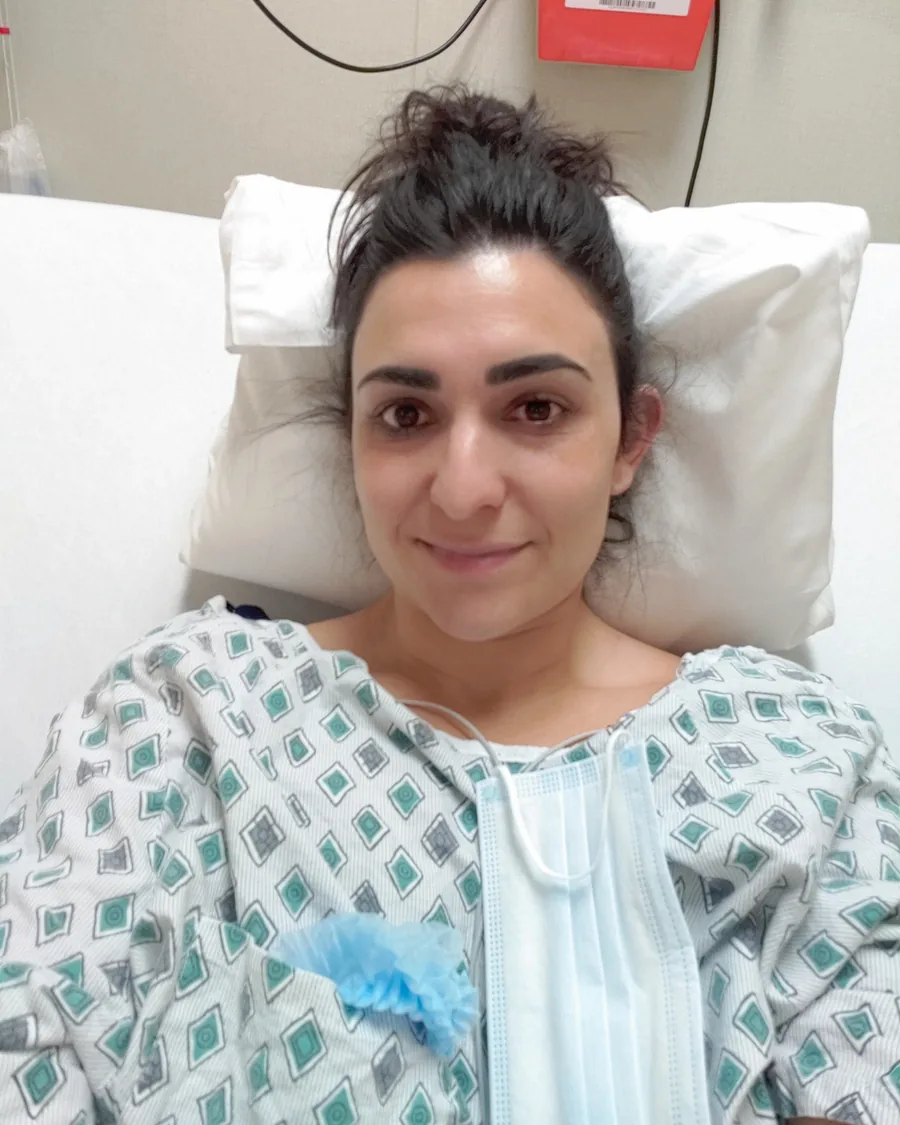 Dr. Christina in a hospital gown, smiling from a hospital bed before knee surgery