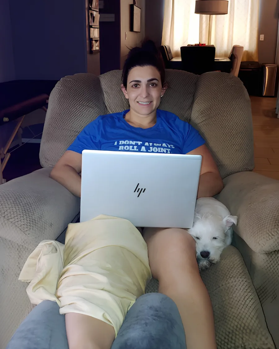 Dr. Christina recovering at home in a recliner, laptop on her lap and her dog beside her