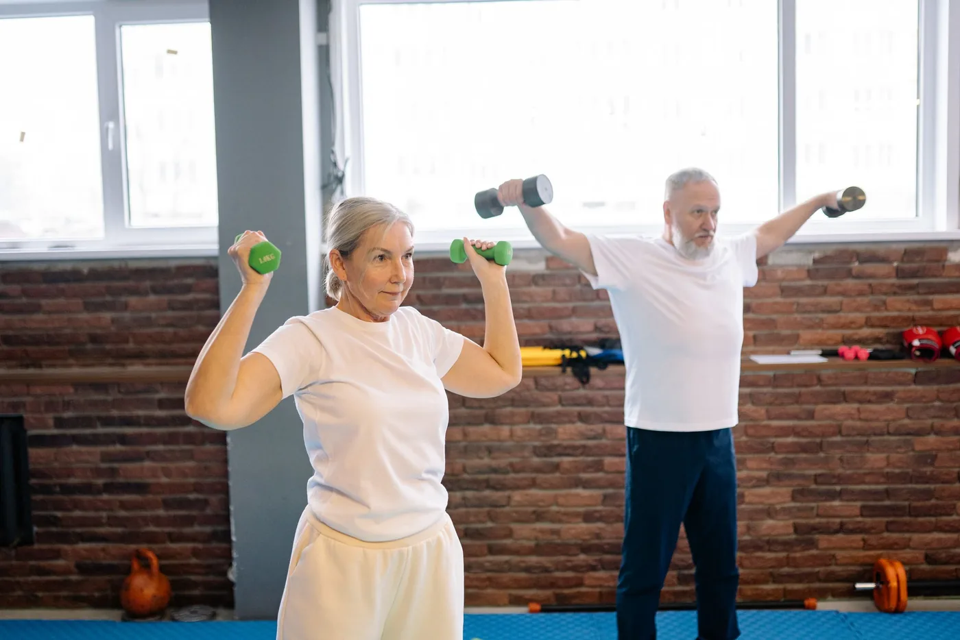 An older couple lifting dumbbells together in a bright gym