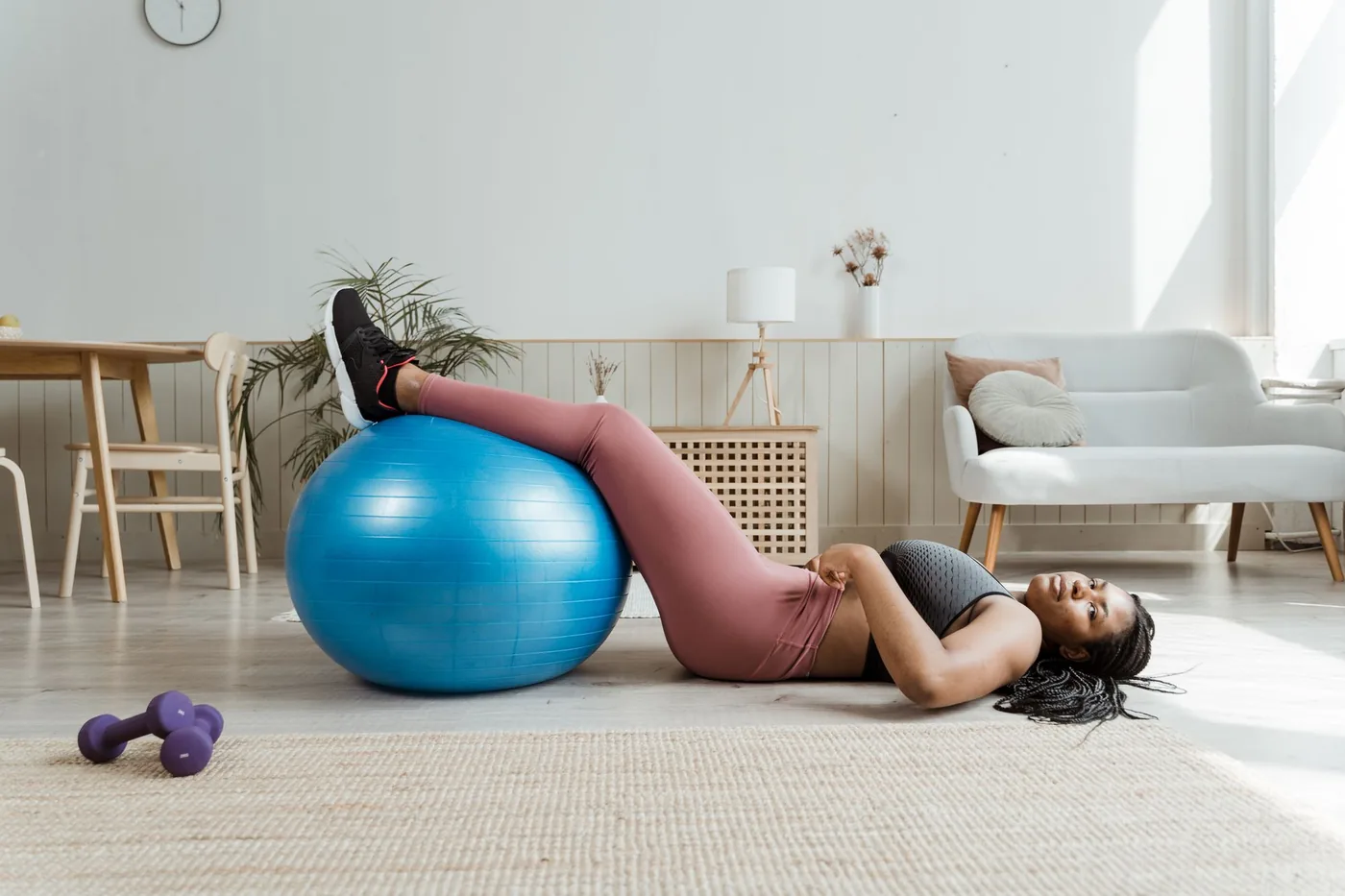 A woman lying on her living room floor with her legs resting on an exercise ball
