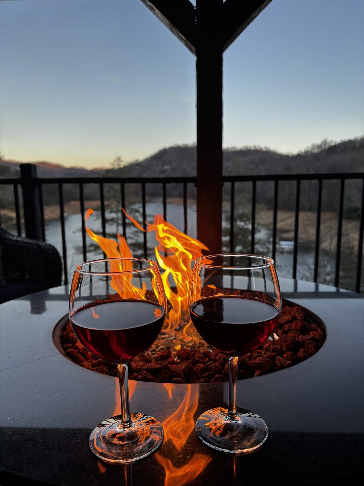 Two glasses of red wine beside a fire pit overlooking the mountains at dusk