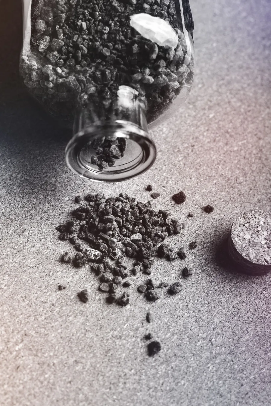 Black-and-white photo of activated charcoal granules spilling from a glass jar onto a table