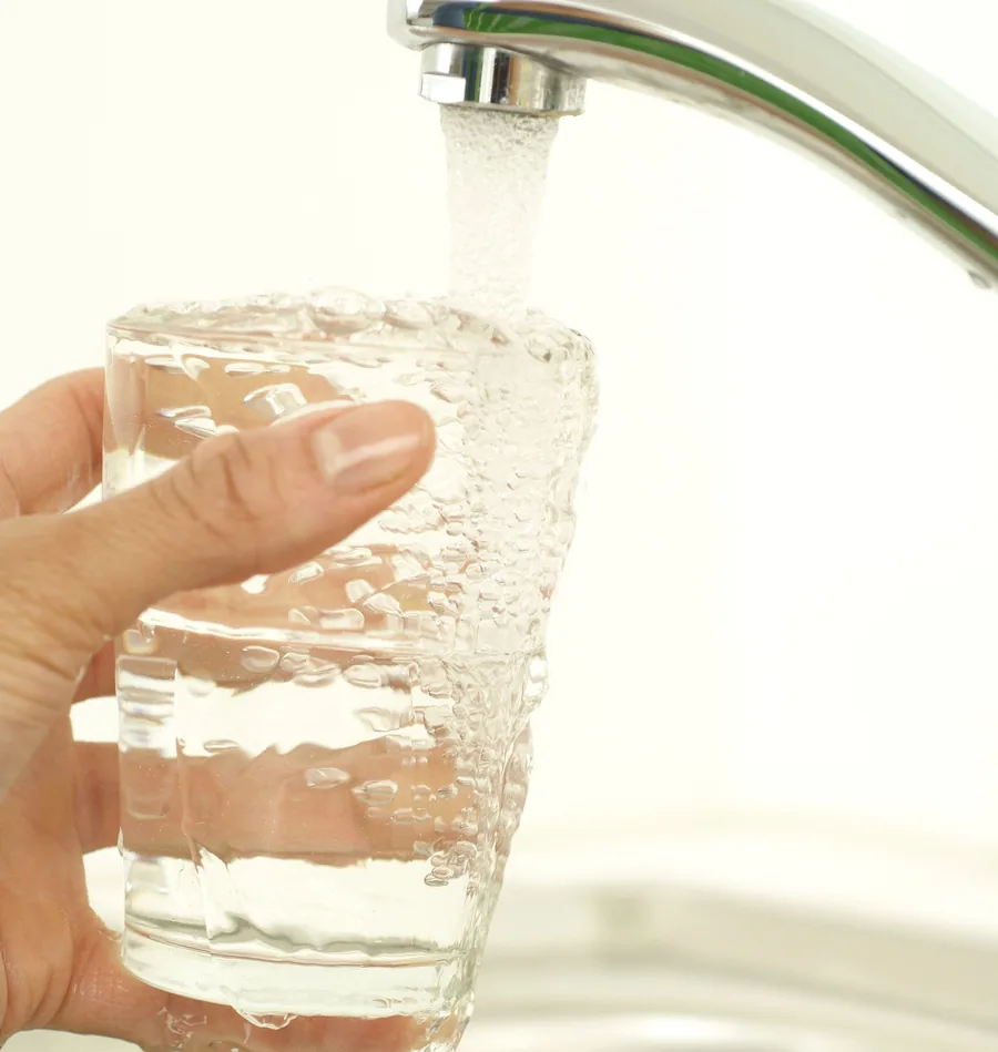 Hand holding a glass as it fills with water from a kitchen faucet