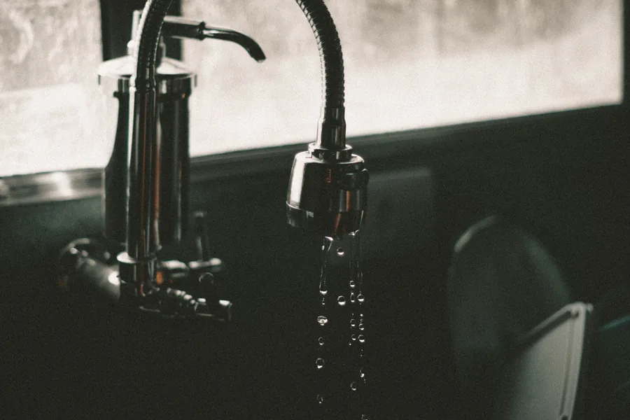 Close-up of a dark kitchen faucet with water droplets falling into the sink
