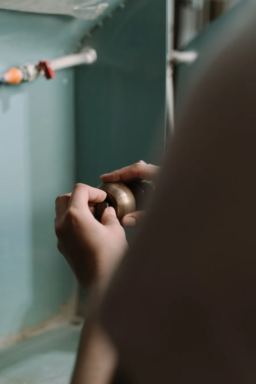 Close-up of hands working on a brass fitting inside a cabinet with water supply pipes and a shutoff valve