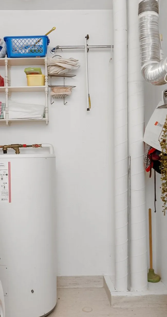 Utility closet with a white water heater tank, a hose reel and exposed plumbing lines