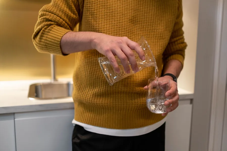 Person pouring water from a pitcher into drinking glasses at a kitchen counter