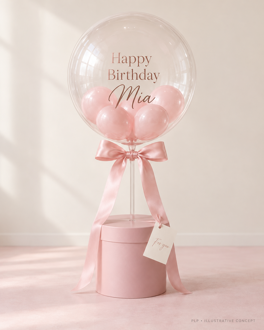 Illustrative clear bubble balloon filled with tiny pink balloons, mounted above a blush decorative base with a satin bow and message card.