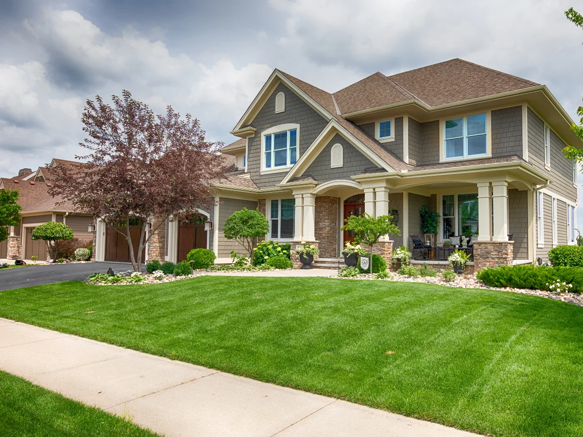 A large, beautiful two-story home with a green lawn and long driveway on a bright, sunny day.