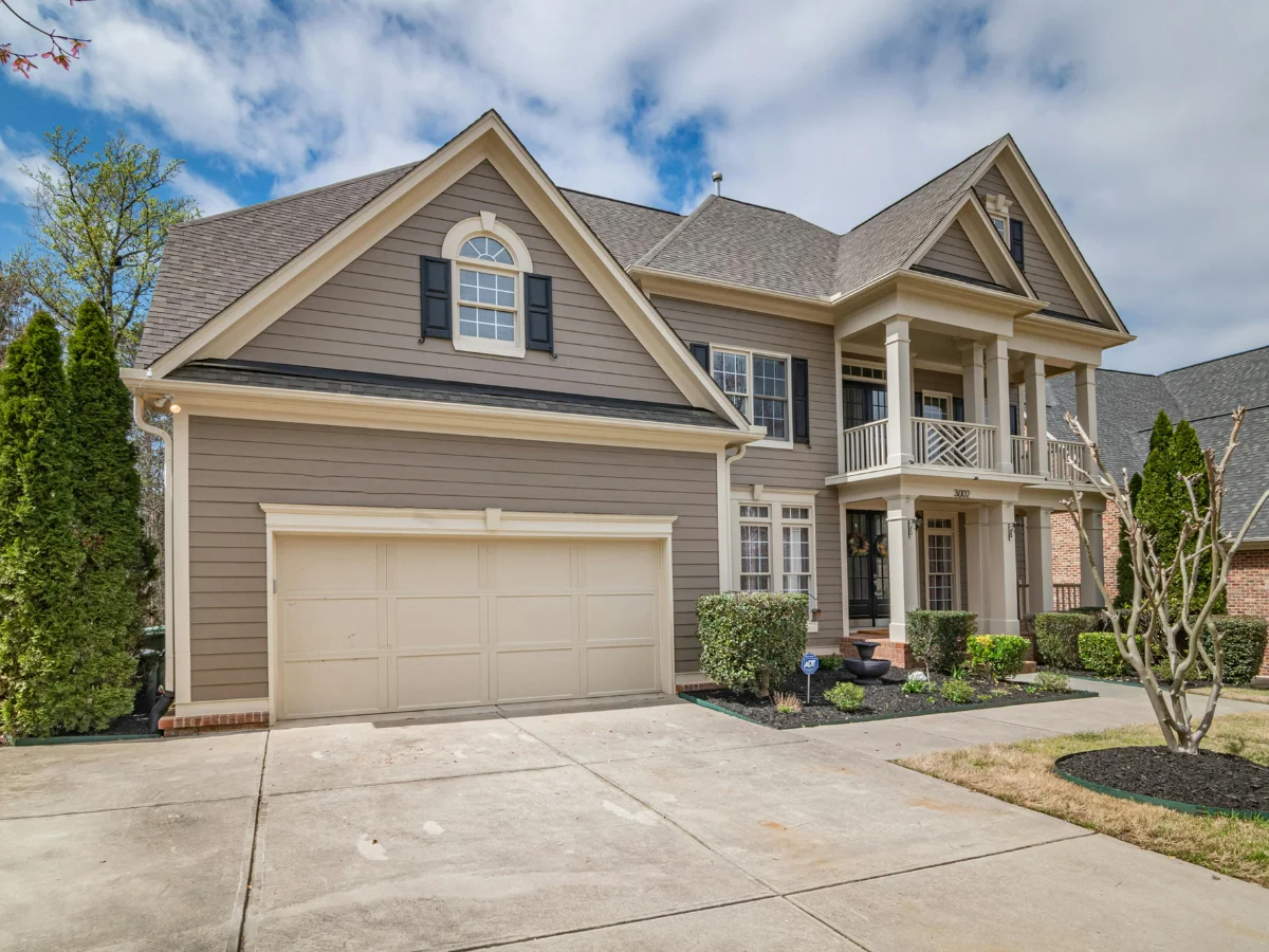 A wide full exterior shot of a large two-story luxury home featuring beige siding, tall white columns, and an expansive driveway.