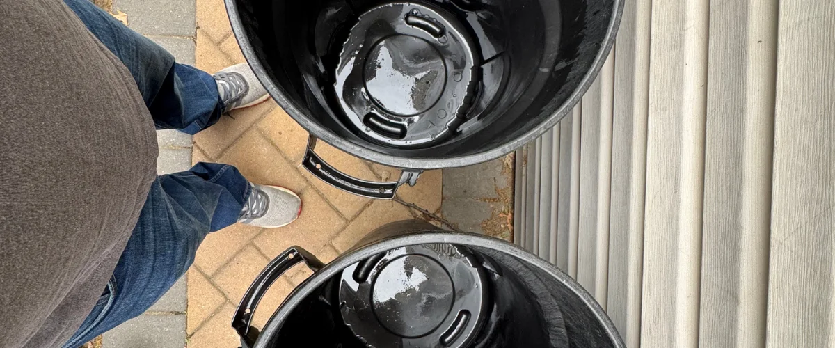Overhead view of a person standing between two large black bins with liquid inside, on a brick patio next to a house. Overhead view of a person standing between two large black bins with liquid inside, on a brick patio next to a house.