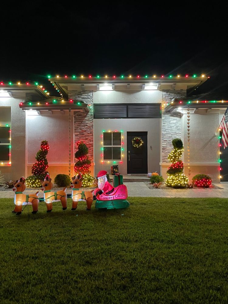 Home with red, green, and white roofline, window outlines, and lit topiaries