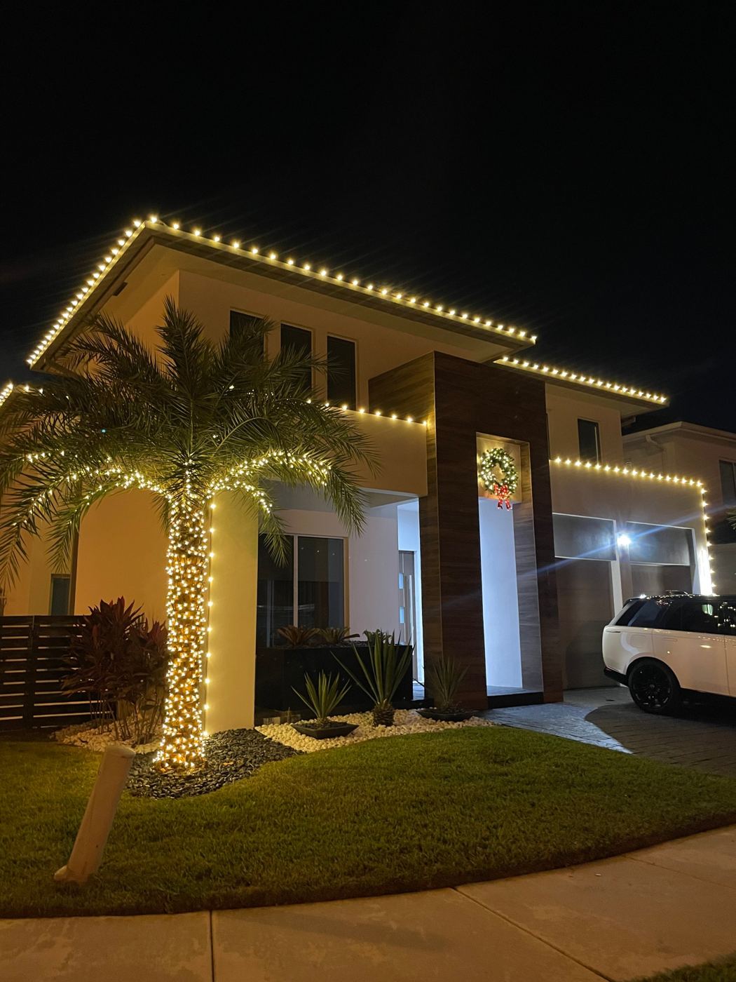 Modern two-story home with warm white roofline lights and a fully wrapped palm tree, installed by Altek