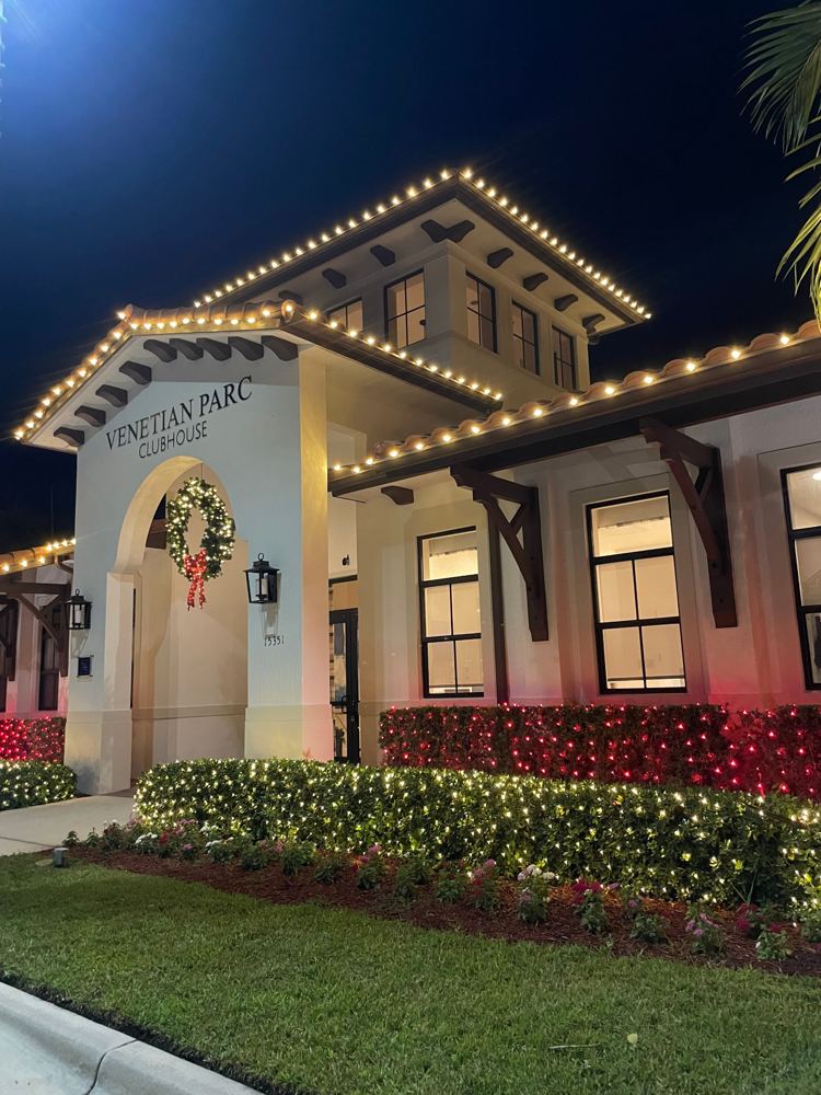 Clubhouse entrance with warm white roofline, wreath, and lit hedges