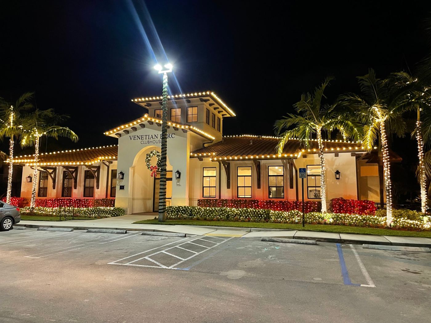 Venetian Parc clubhouse with warm white rooflines, wrapped palms, and red and white hedges