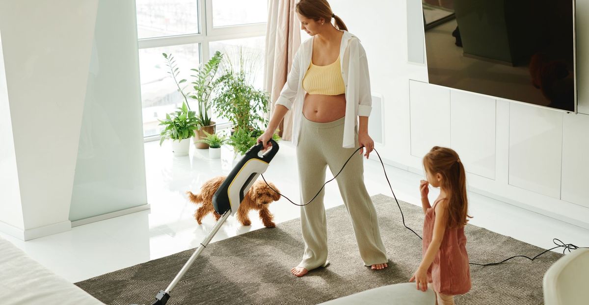 Woman vacuuming a rug in a bright Vancouver living room while a child and a small dog look on