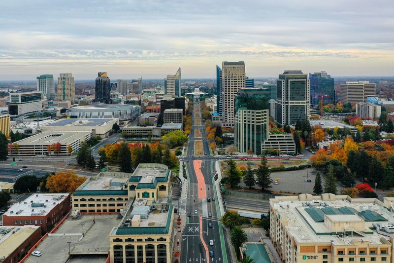 An aerial view of downtown Sacramento, with a central avenue leading toward the skyline and autumn-colored trees.