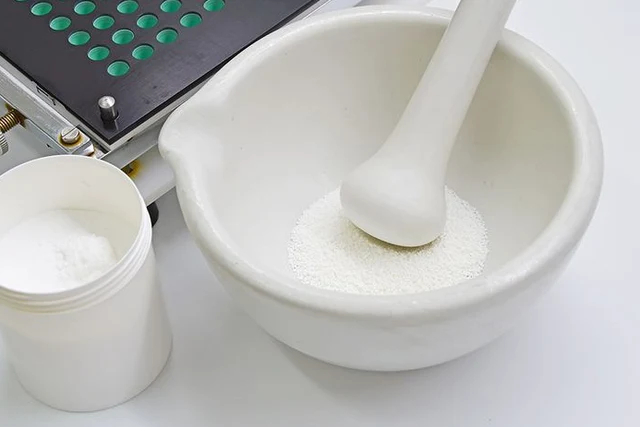 White powder in a mortar with a pestle beside a compounding device and container.