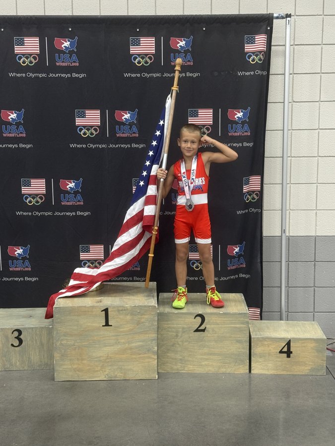 NoWorries Academy wrestler on the podium with USA Wrestling flag